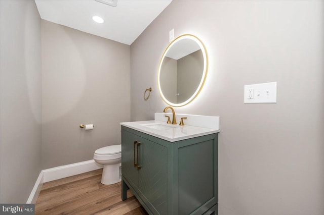 half bath featuring vanity, baseboards, toilet, and wood finished floors