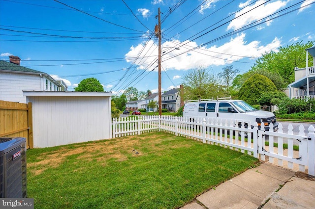 view of yard with a residential view, a fenced front yard, central AC, and driveway