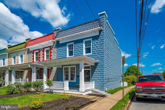view of front facade with covered porch, a chimney, and a tile roof
