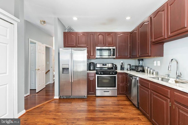 kitchen with appliances with stainless steel finishes, dark wood-style flooring, light stone countertops, and a sink