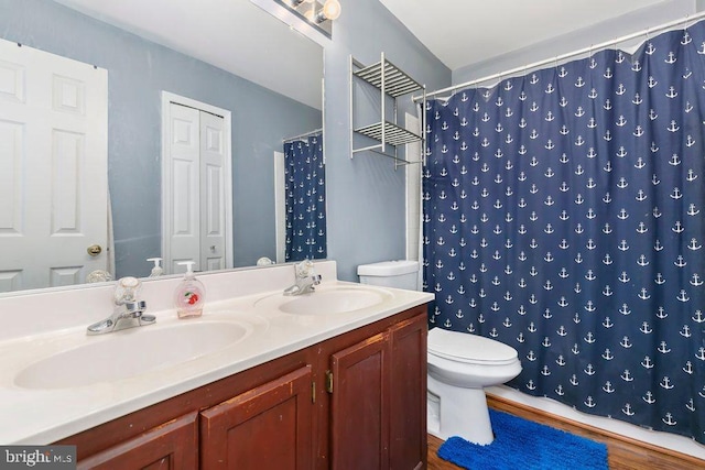 bathroom featuring toilet, double vanity, a sink, and wood finished floors