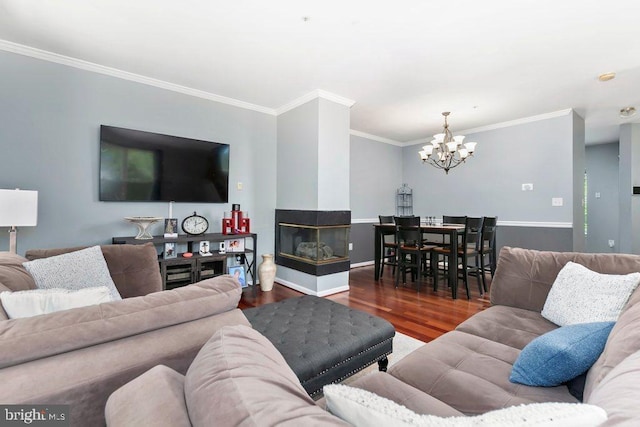 living area featuring an inviting chandelier, ornamental molding, baseboards, and wood finished floors