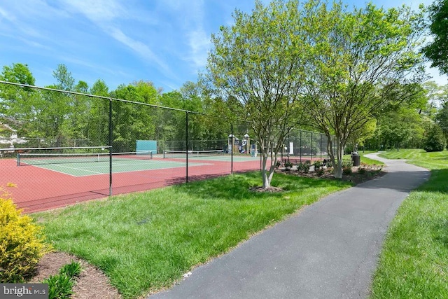 view of tennis court featuring a lawn and fence