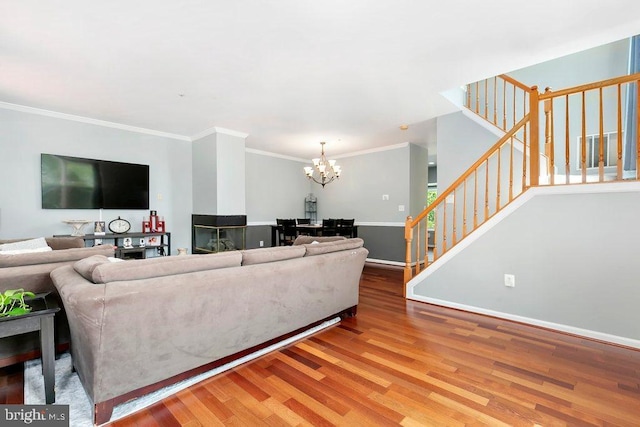 living room featuring a notable chandelier, baseboards, stairs, crown molding, and wood finished floors