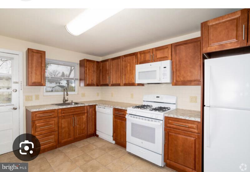 kitchen with white appliances, brown cabinetry, a sink, and tasteful backsplash