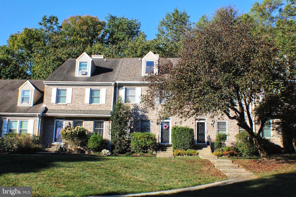 view of front of home featuring a shingled roof, a front lawn, and brick siding