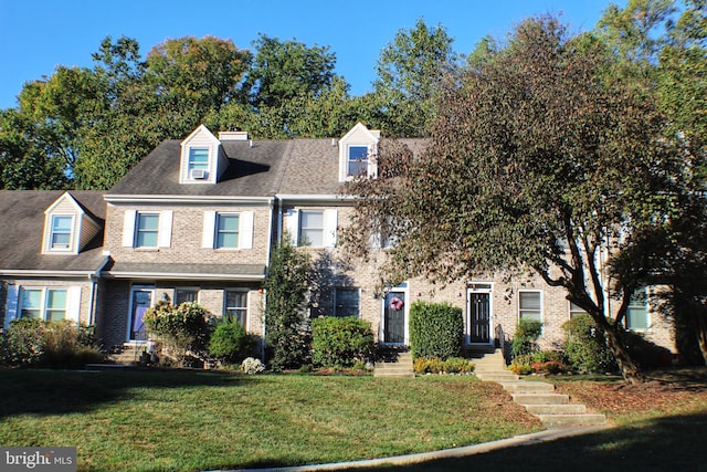 view of front of home featuring a shingled roof, a front lawn, and brick siding