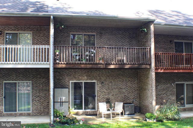 rear view of property featuring a balcony, central AC, a patio area, and brick siding