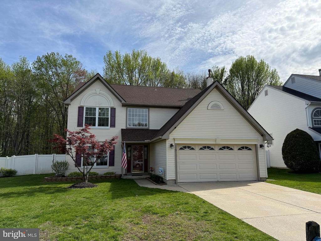 traditional-style home featuring driveway, fence, a front lawn, and a garage