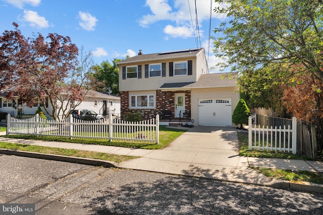 colonial-style house with driveway, a fenced front yard, roof mounted solar panels, and a garage