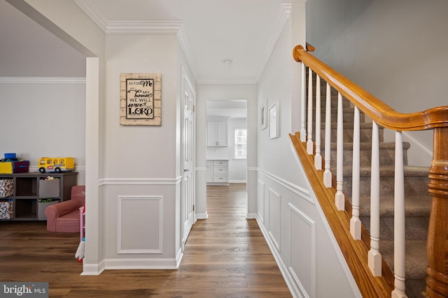 hall with ornamental molding, a decorative wall, stairs, and wood finished floors