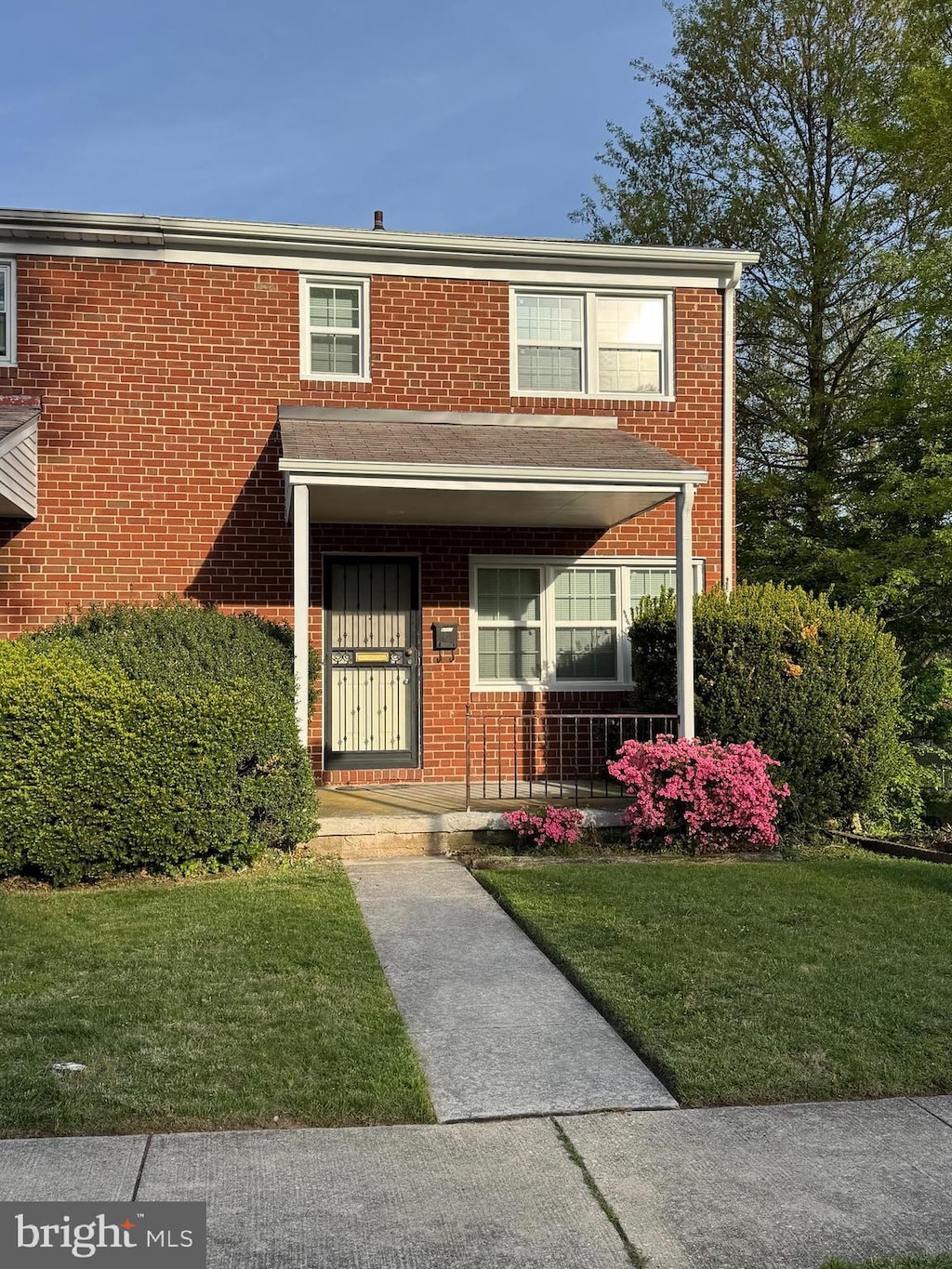 view of property with brick siding, covered porch, and a front yard