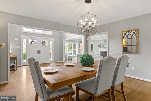 dining space featuring an inviting chandelier, light wood-style floors, a glass covered fireplace, and baseboards