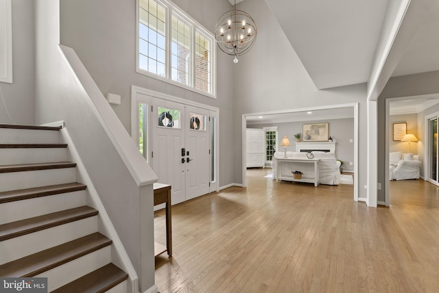 entryway with a high ceiling, a notable chandelier, light wood-style flooring, stairs, and baseboards