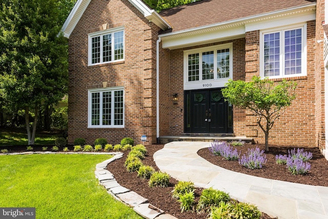 view of exterior entry featuring brick siding and a yard