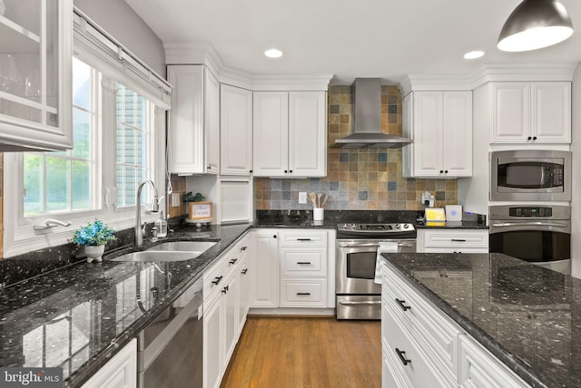 kitchen with a sink, wall chimney exhaust hood, appliances with stainless steel finishes, and white cabinetry