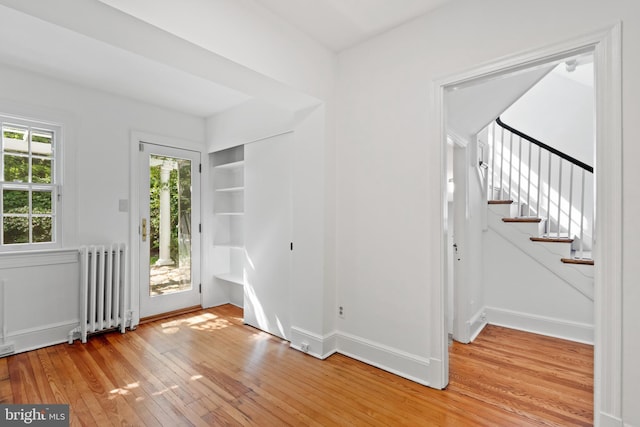 foyer entrance featuring radiator heating unit, baseboards, stairs, and light wood-style flooring