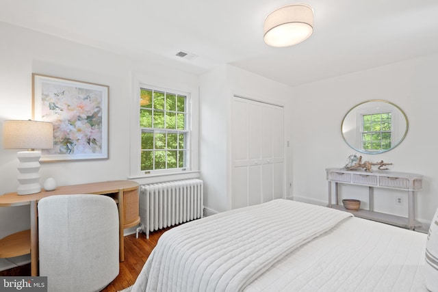 bedroom with visible vents, radiator heating unit, a closet, and wood finished floors
