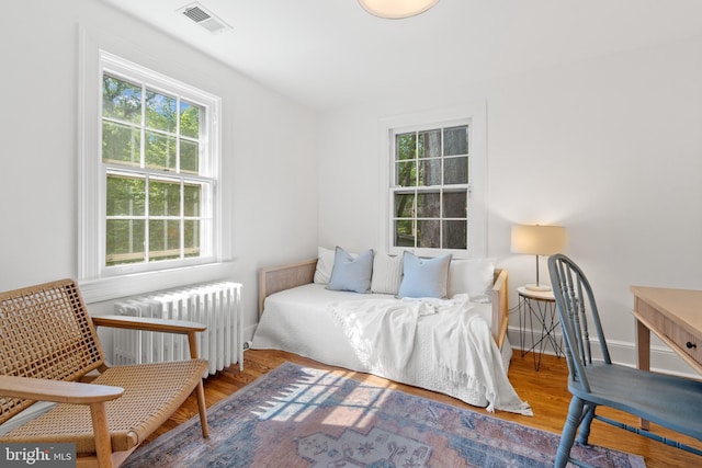 bedroom featuring visible vents, radiator heating unit, multiple windows, and wood finished floors