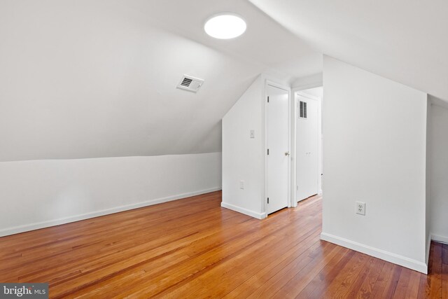 additional living space with baseboards, lofted ceiling, light wood-type flooring, and visible vents
