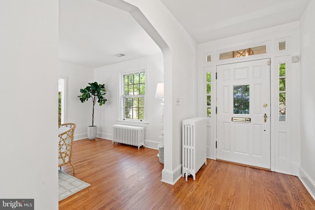 foyer featuring radiator, baseboards, arched walkways, and wood finished floors