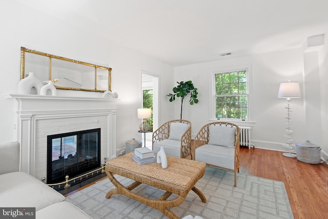 living area with visible vents, wood finished floors, a fireplace, baseboards, and radiator heating unit