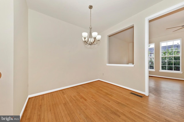 spare room with hardwood / wood-style flooring, a chandelier, and baseboards