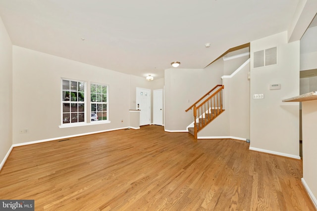 unfurnished living room with stairway, light wood-style flooring, and baseboards