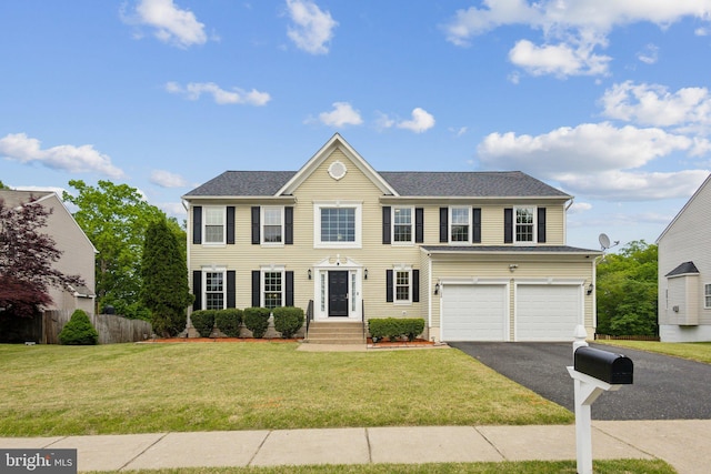 colonial house featuring fence, an attached garage, a front lawn, and aphalt driveway