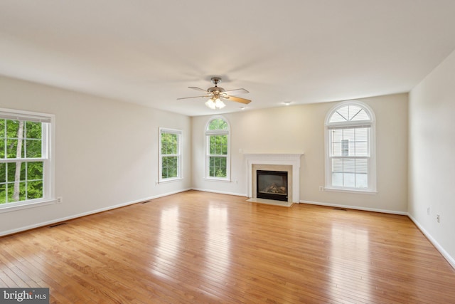 unfurnished living room with ceiling fan, a fireplace with flush hearth, baseboards, and light wood-type flooring