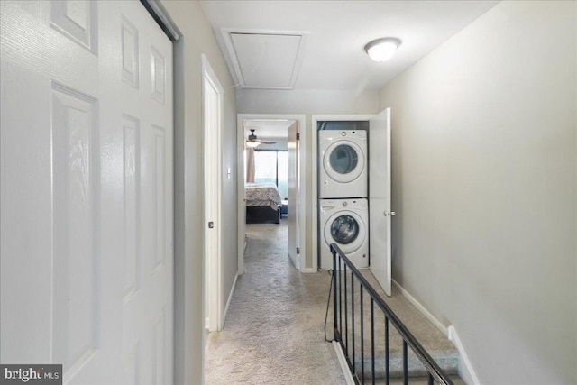 hallway featuring carpet flooring, stacked washing maching and dryer, attic access, baseboards, and an upstairs landing