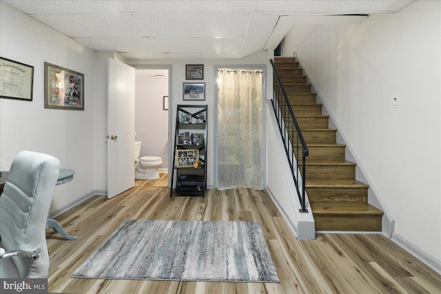 staircase featuring baseboards, a drop ceiling, and wood finished floors