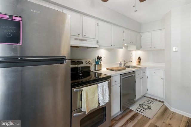 kitchen with under cabinet range hood, white cabinets, a sink, light wood finished floors, and stainless steel appliances