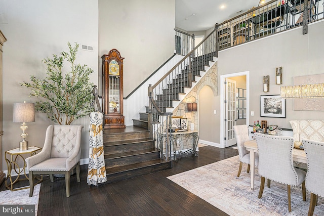 interior space with stairs, baseboards, a towering ceiling, visible vents, and hardwood / wood-style flooring