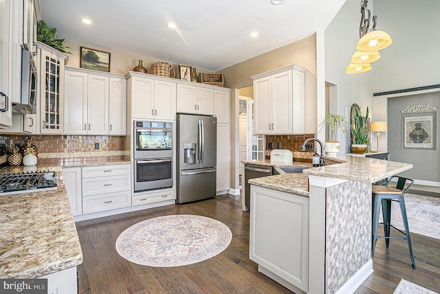 kitchen featuring decorative backsplash, a peninsula, light stone counters, a sink, and stainless steel appliances
