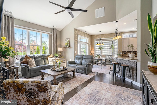 living room featuring high vaulted ceiling, ceiling fan with notable chandelier, dark wood-type flooring, and visible vents