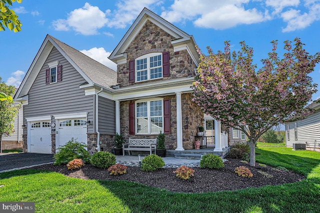 view of front facade featuring a front lawn, aphalt driveway, covered porch, stone siding, and an attached garage