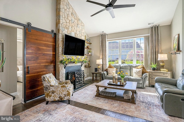 living room with ceiling fan, a stone fireplace, wood finished floors, vaulted ceiling, and visible vents