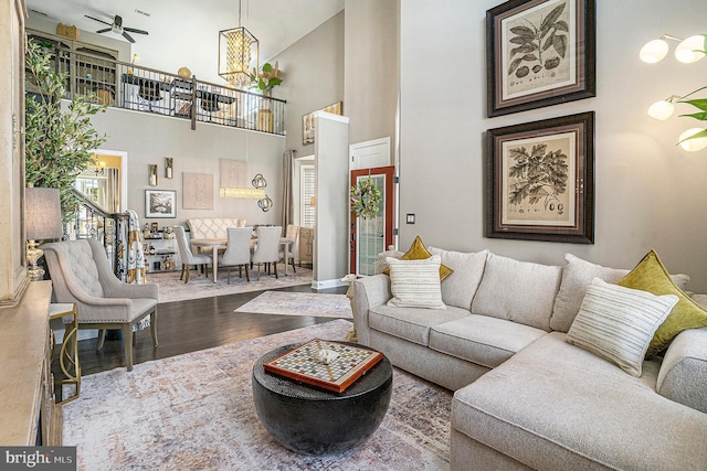 living area with ceiling fan with notable chandelier, a towering ceiling, and wood finished floors
