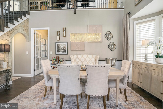 dining area with baseboards, dark wood-type flooring, arched walkways, and a towering ceiling