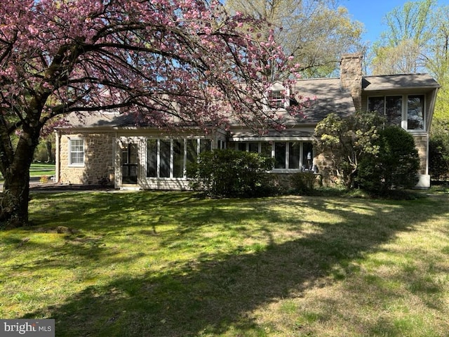 rear view of property featuring a chimney, a lawn, and stone siding