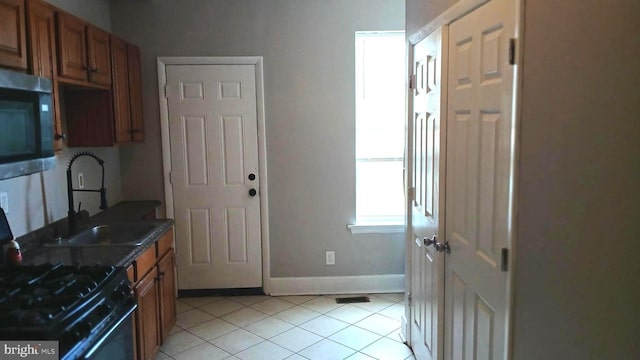 kitchen featuring dark countertops, a sink, stainless steel microwave, light tile patterned floors, and black gas range