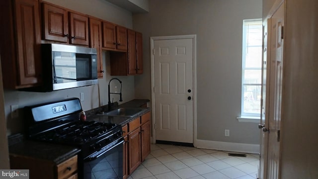 kitchen with light tile patterned flooring, dark countertops, gas range oven, stainless steel microwave, and a sink