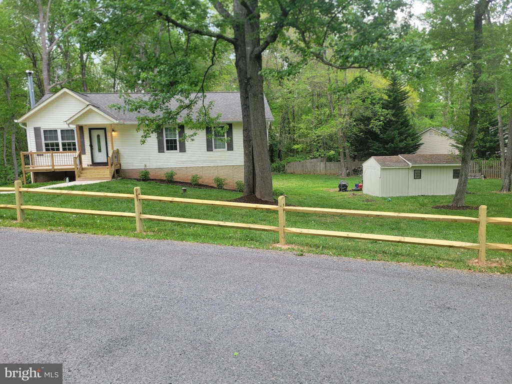 single story home with fence private yard, a front lawn, roof with shingles, a shed, and an outbuilding