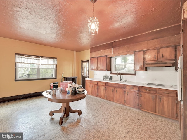 kitchen with brown cabinetry, a textured ceiling, light countertops, under cabinet range hood, and a wealth of natural light