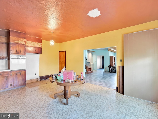 interior space featuring hanging light fixtures, light countertops, brown cabinetry, baseboards, and white oven