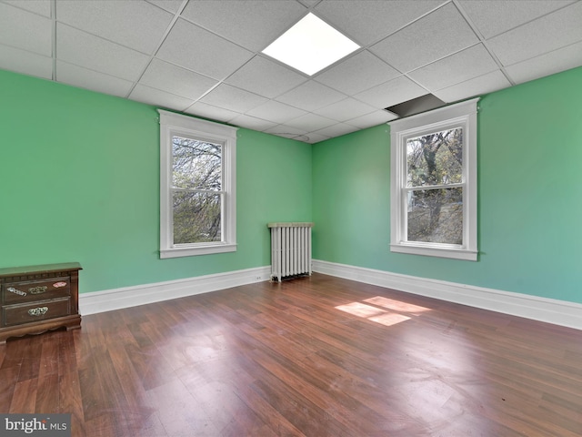 empty room with baseboards, a paneled ceiling, wood finished floors, and radiator heating unit