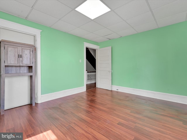 unfurnished room with baseboards, a paneled ceiling, and wood finished floors