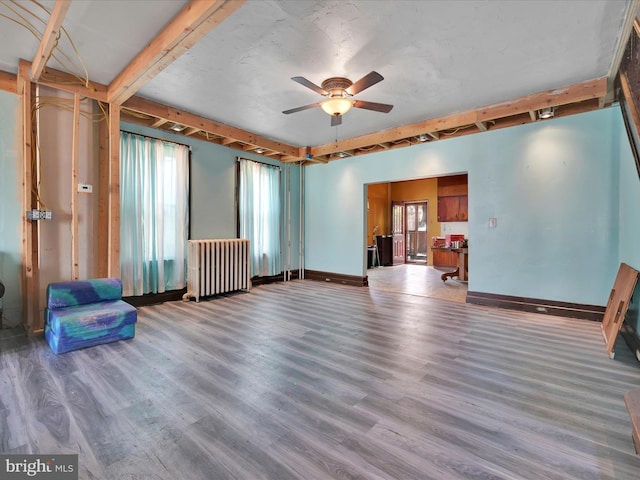 unfurnished living room featuring a ceiling fan, wood finished floors, baseboards, beamed ceiling, and radiator heating unit