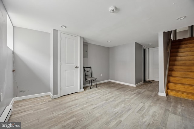 finished basement with baseboards, light wood-style flooring, baseboard heating, and stairway